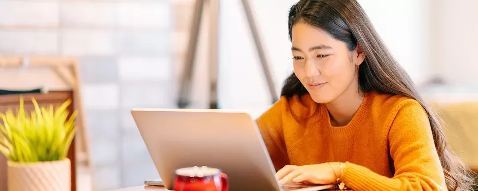 オレンジ色のセーターを着た女性がデスクでノートパソコンを使っています。