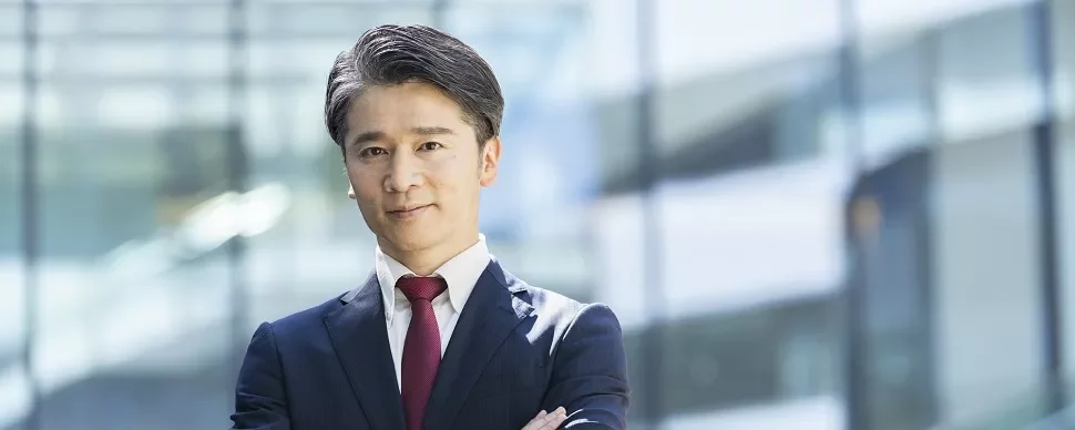 スーツ姿で腕を組んだビジネスマンがオフィスにいる。