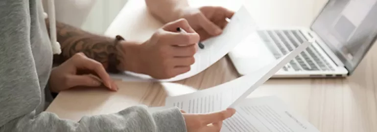 ラップトップの近くで書類を見ている2人の人。