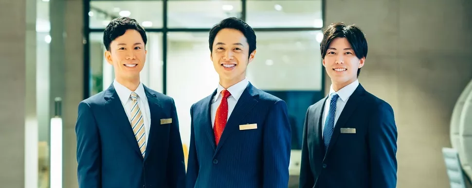 ロビーでスーツを着た3人の男性がカメラに向かって微笑んでいる。