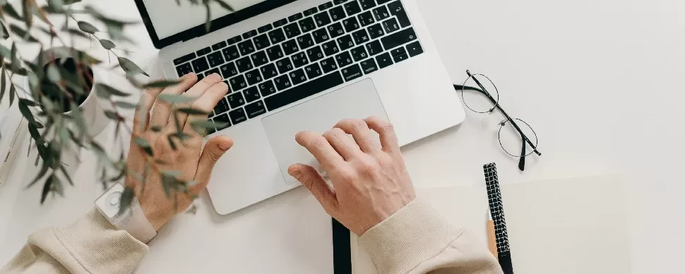 Person working on a laptop with notepad and glasses nearby
