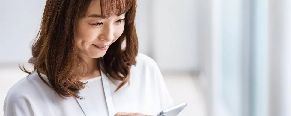 明るい部屋でスマホを見て微笑む女性。