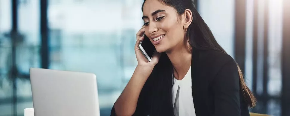 Woman smiling while talking on the phone and using a laptop.