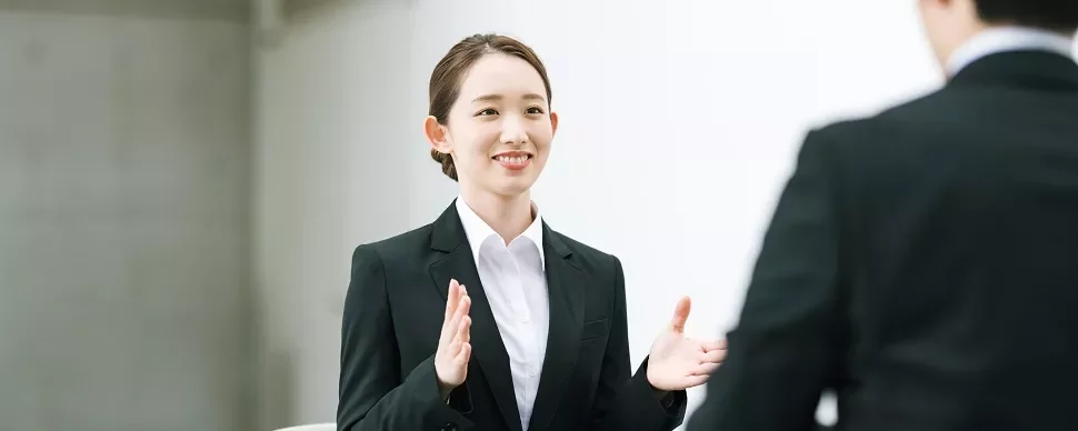 会議中に笑顔でジェスチャーをしているビジネススーツの女性。