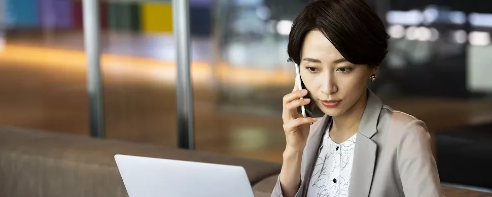 オフィスで電話しながらノートパソコンを使う女性。