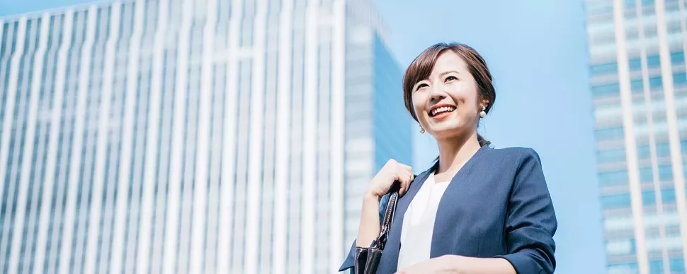 Woman smiling outdoors in business attire with skyscrapers in the background.
