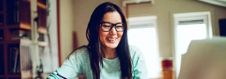 眼鏡をかけた女性がコンピュータを見ながら微笑んでいる。