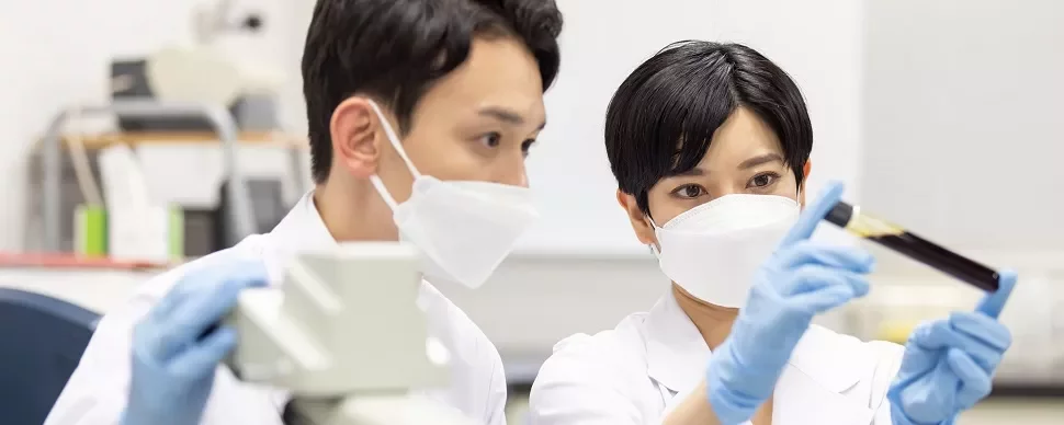 研究室でマスクをした2人の科学者が試験管を調べています。