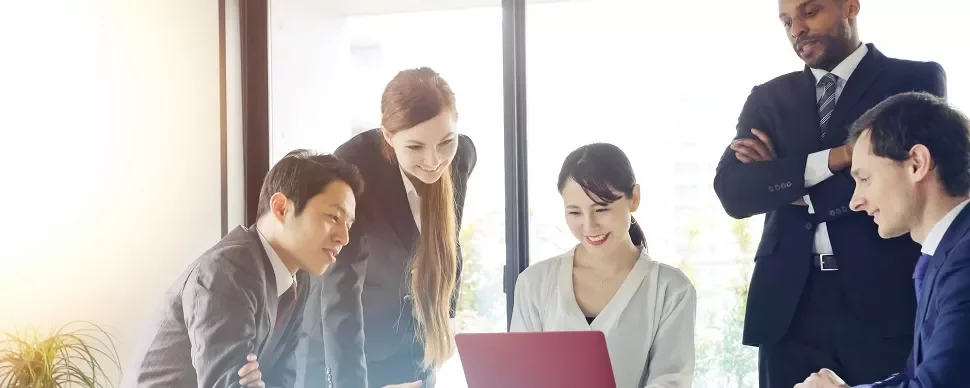 明るいオフィスでノートパソコンを見ている多様な職業のグループ。