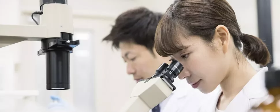研究者がラボで顕微鏡を使ってサンプルを調べています。