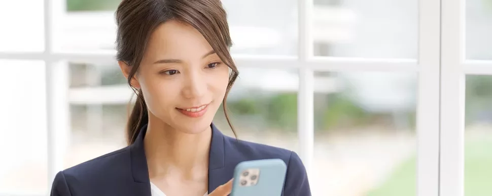窓辺でスマートフォンを見ている女性。