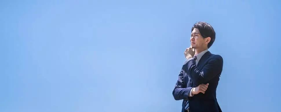 青空の下で考えるスーツ姿の人。