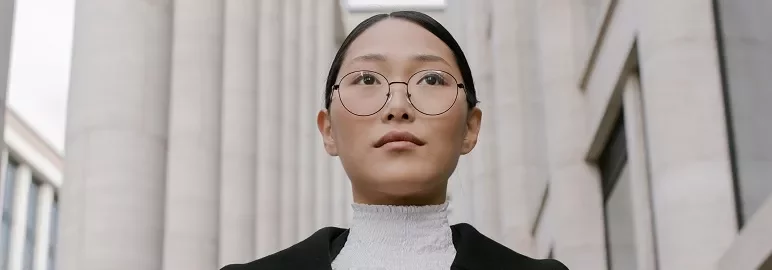 丸い眼鏡をかけた人物が高い柱の前に立っている。