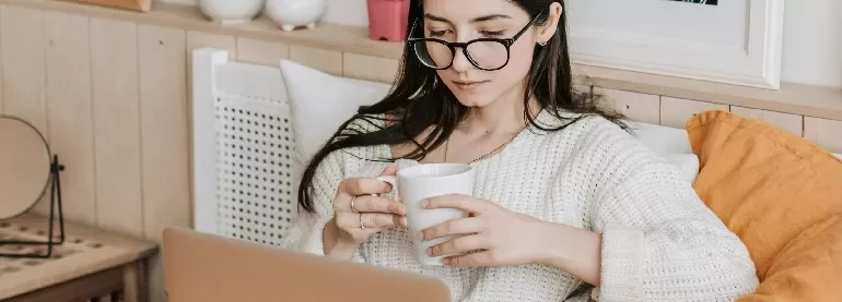 女性がラップトップを使いながらコーヒーを飲んでいる。