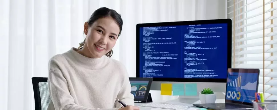 コンピュータ画面にコードとグラフを表示して微笑む女性。