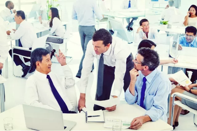 Colleagues in an open office space discuss work while others focus on their tasks.