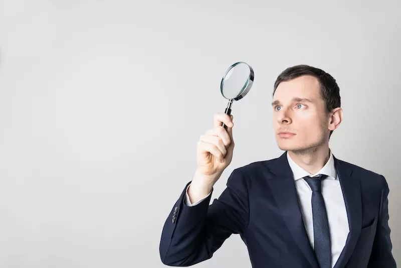 Man in suit using magnifying glass, looking upwards.