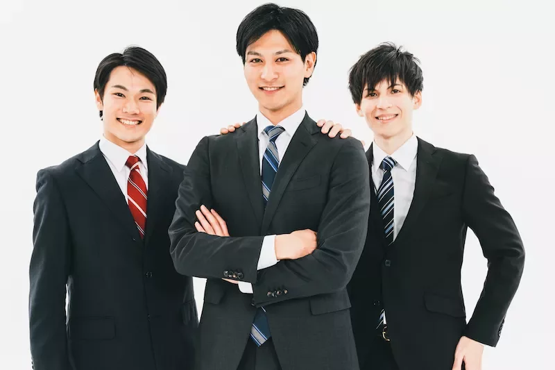 スーツを着た3人が笑顔でポーズを取っています。