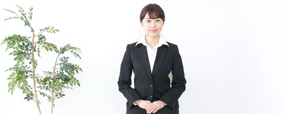 黒いスーツを着た女性が鉢植えの植物の横に座っています。