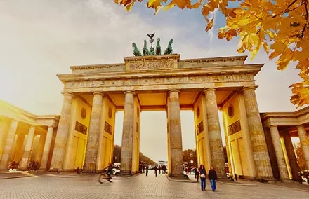 The Brandenburg Gate with autumn leaves and people walking.