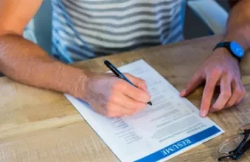 Person writing on a resume at a desk.