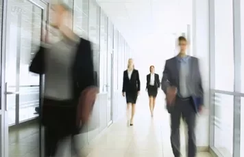 Blurred image of people walking in an office corridor.