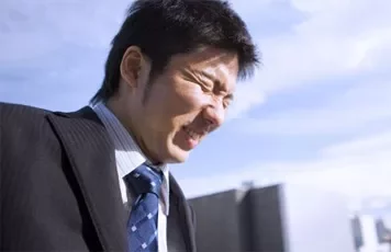 Man squinting in sunlight in front of buildings.