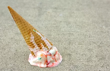 Ice cream cone fallen on the ground with colorful toppings melting.