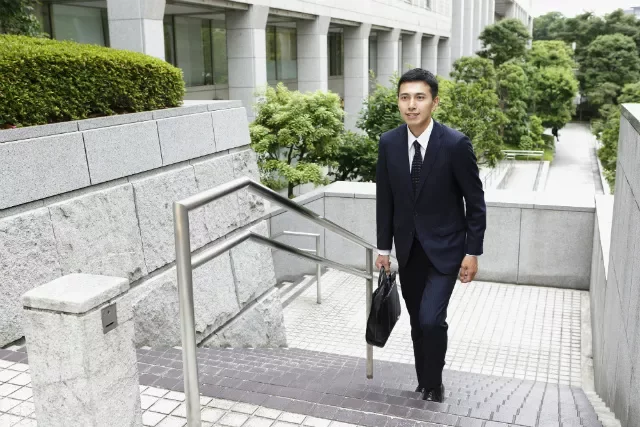 Man in a suit walking up outdoor stairs, carrying a briefcase.