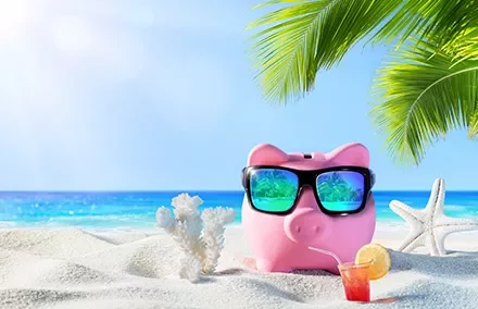 Piggy bank with sunglasses on tropical beach with cocktail