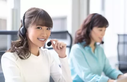 Two women using headsets in an office setting, one smiling at the camera.