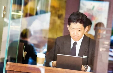 カフェでタブレットを使うスーツ姿の男性。テーブルにはコーヒーカップ。