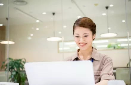 Woman smiling while using a laptop in a bright office.
