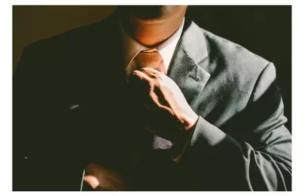 Man adjusting his tie in a suit, shadowed lighting.