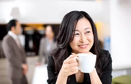 Woman smiling with a cup of coffee in an office setting.
