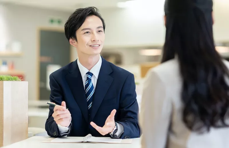 スーツの男性が女性と円卓で会話をしている。