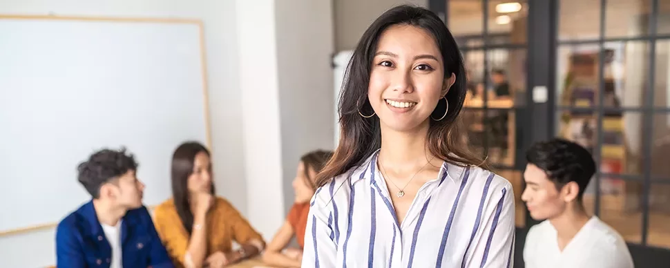 Woman smiling in office meeting, four people in background.
