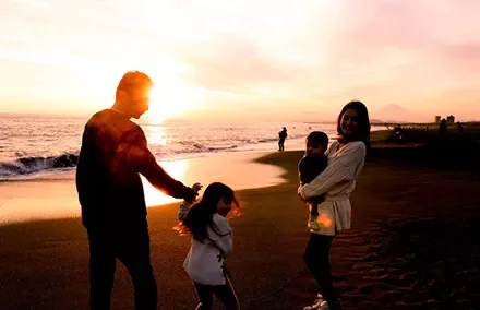 Family enjoying sunset at the beach with ocean waves in the background.