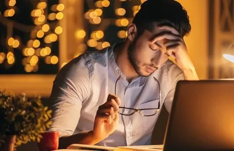 Man looking tired while working on a laptop at night.
