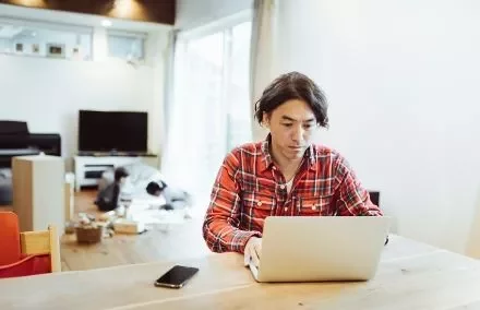 Person working on a laptop at a wooden table in a cozy living room.