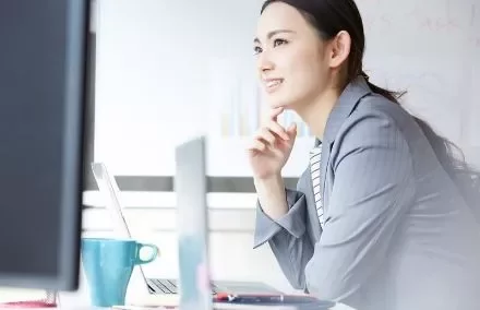 Woman in business attire working at a desk with a laptop.