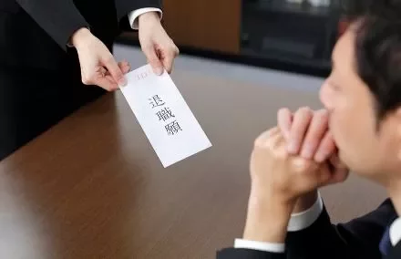 Person hands over a resignation letter to another person seated at a table.
