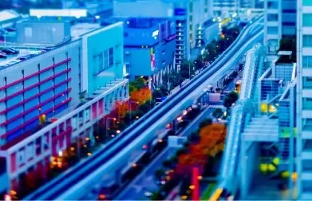 Aerial view of a vibrant cityscape with tilt-shift effect, blue buildings, and autumn trees lining the street.
