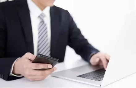 Business person using a smartphone and laptop at a desk.