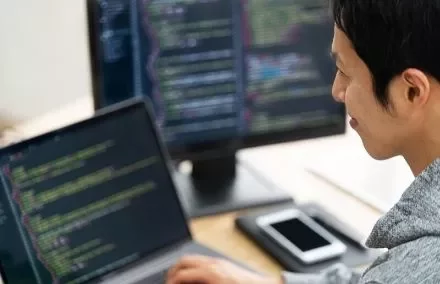 Person coding on a laptop with another screen in the background, focused on software development.