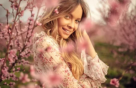 Woman smiling amid blooming pink flowers in a garden.