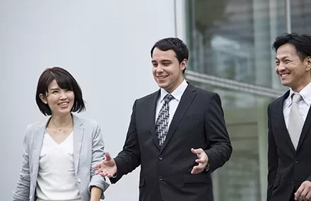 Three business professionals in suits walking outside, having a conversation.