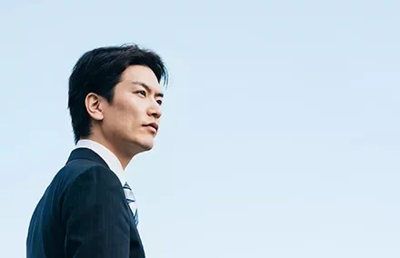 Man in a suit looking ahead against a clear blue sky.