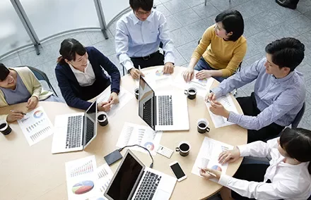 Team meeting at an office table with laptops and documents.