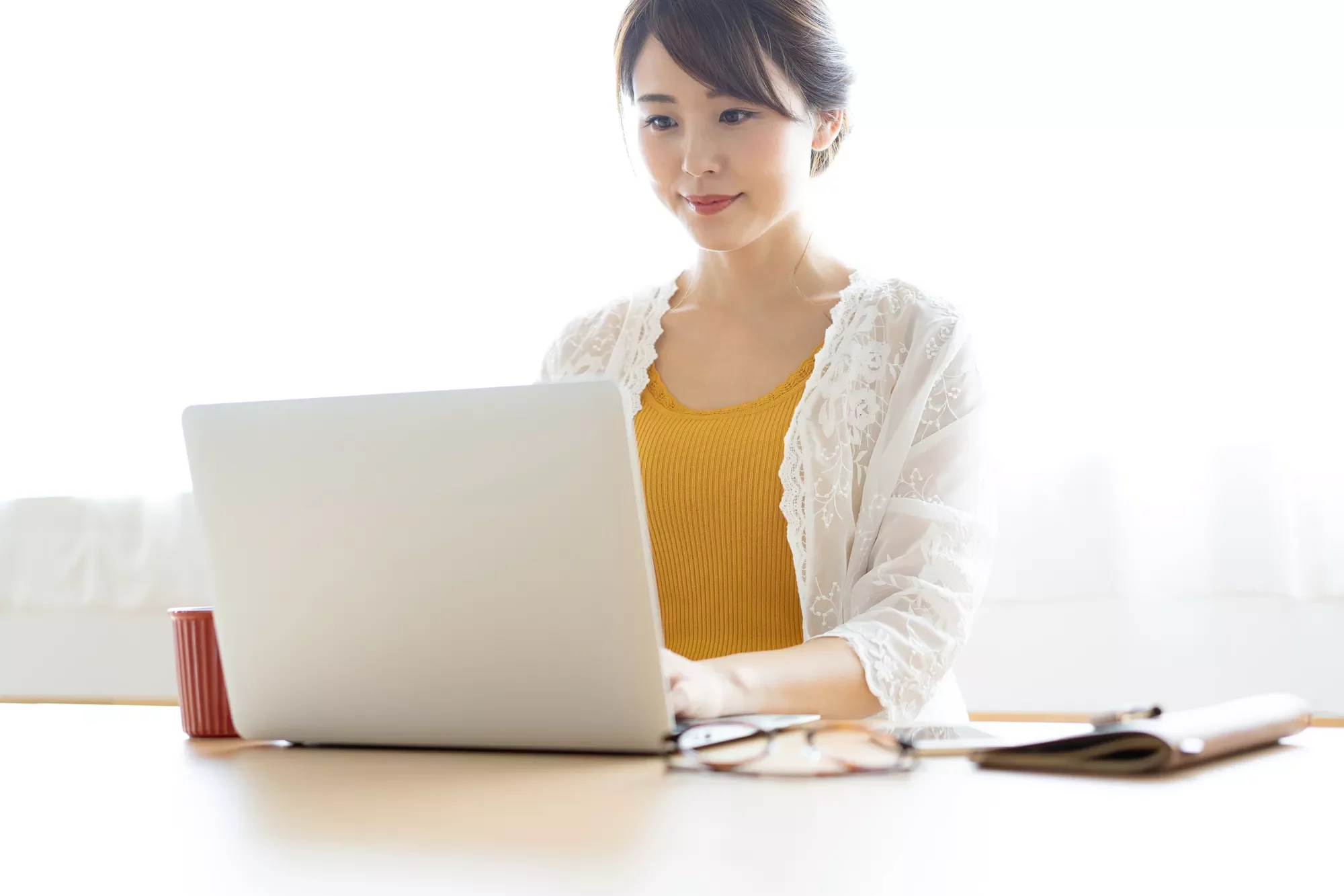 Person working on a laptop at a desk with a cup and glasses nearby.
